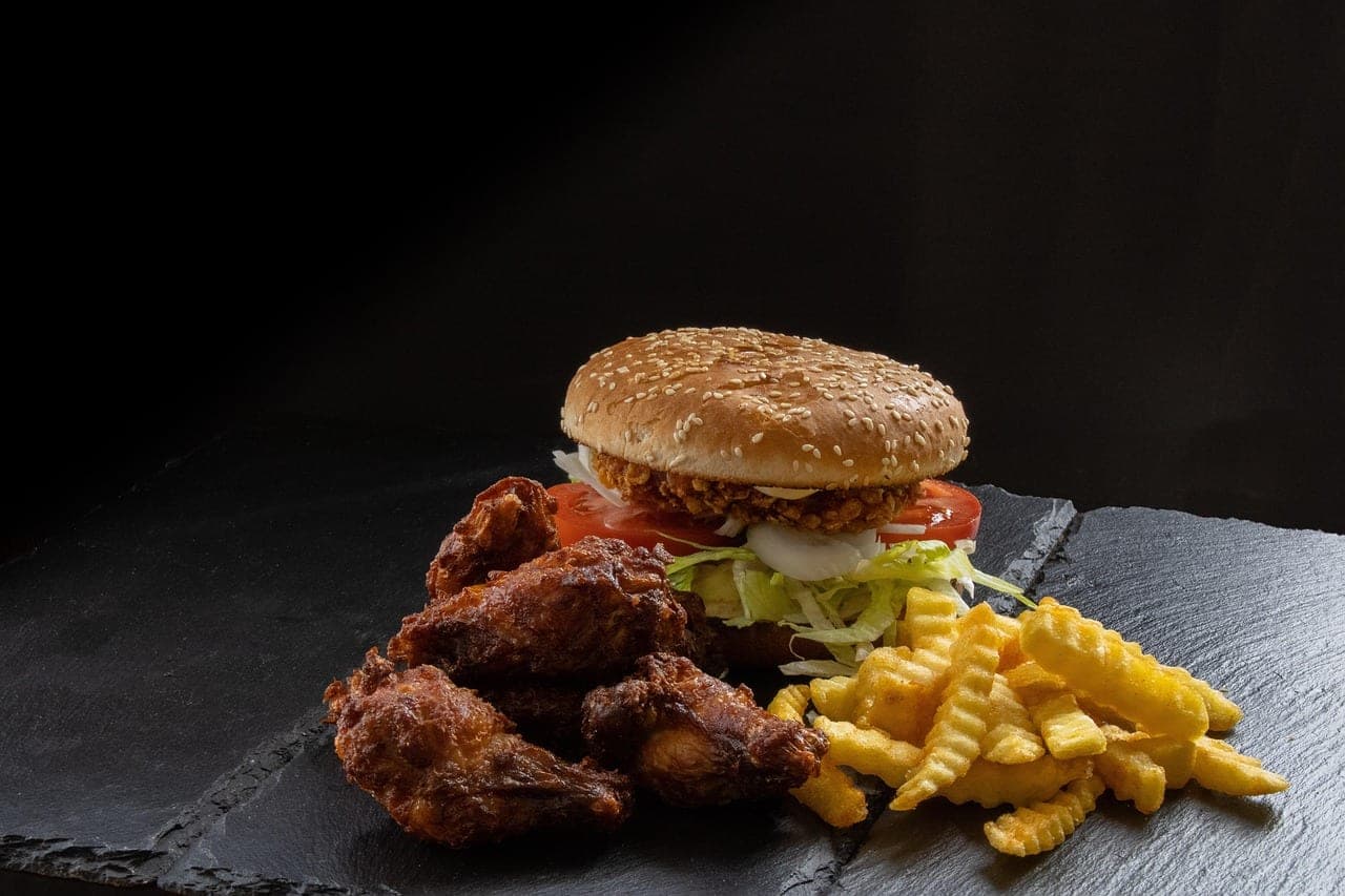 A breaded chicken burger with fried wings and fries, on a slate board.