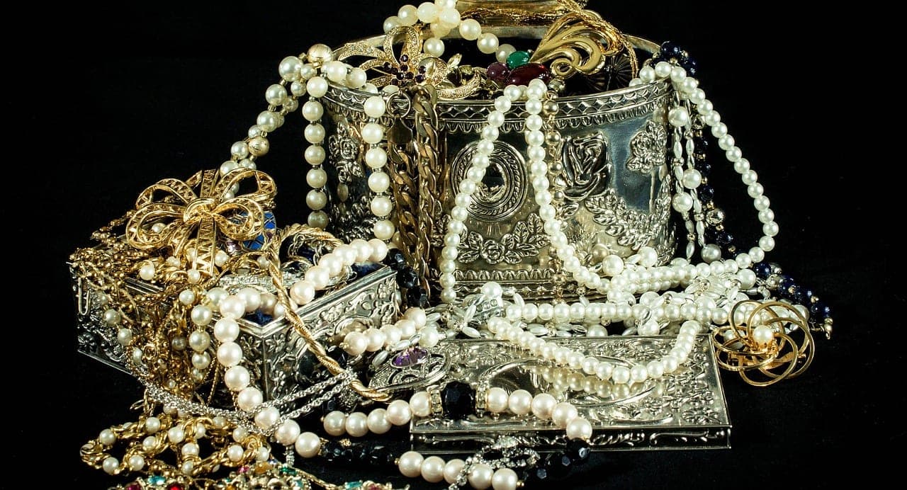 Pearl necklaces, gold brooches and chased silver boxes heaped on a black background.