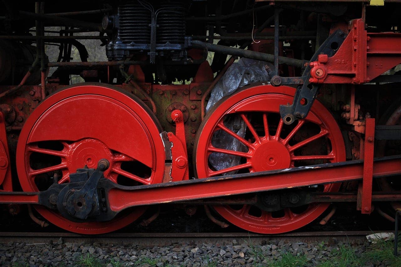The red driving wheels of an old steam locomotive, with its coupling rod.