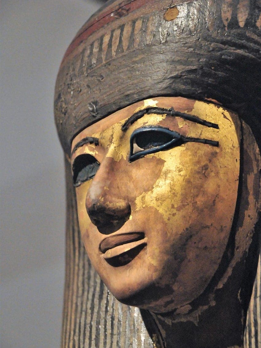 The gilded face of an Egyptian sarcophagus, its eyes outlined in black.
