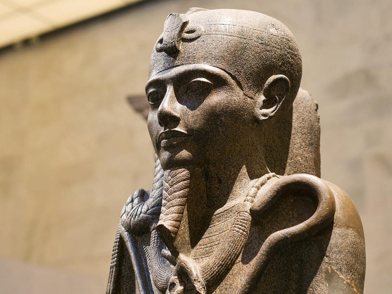 A granite pharaonic statue seen in profile, in a bright hall.