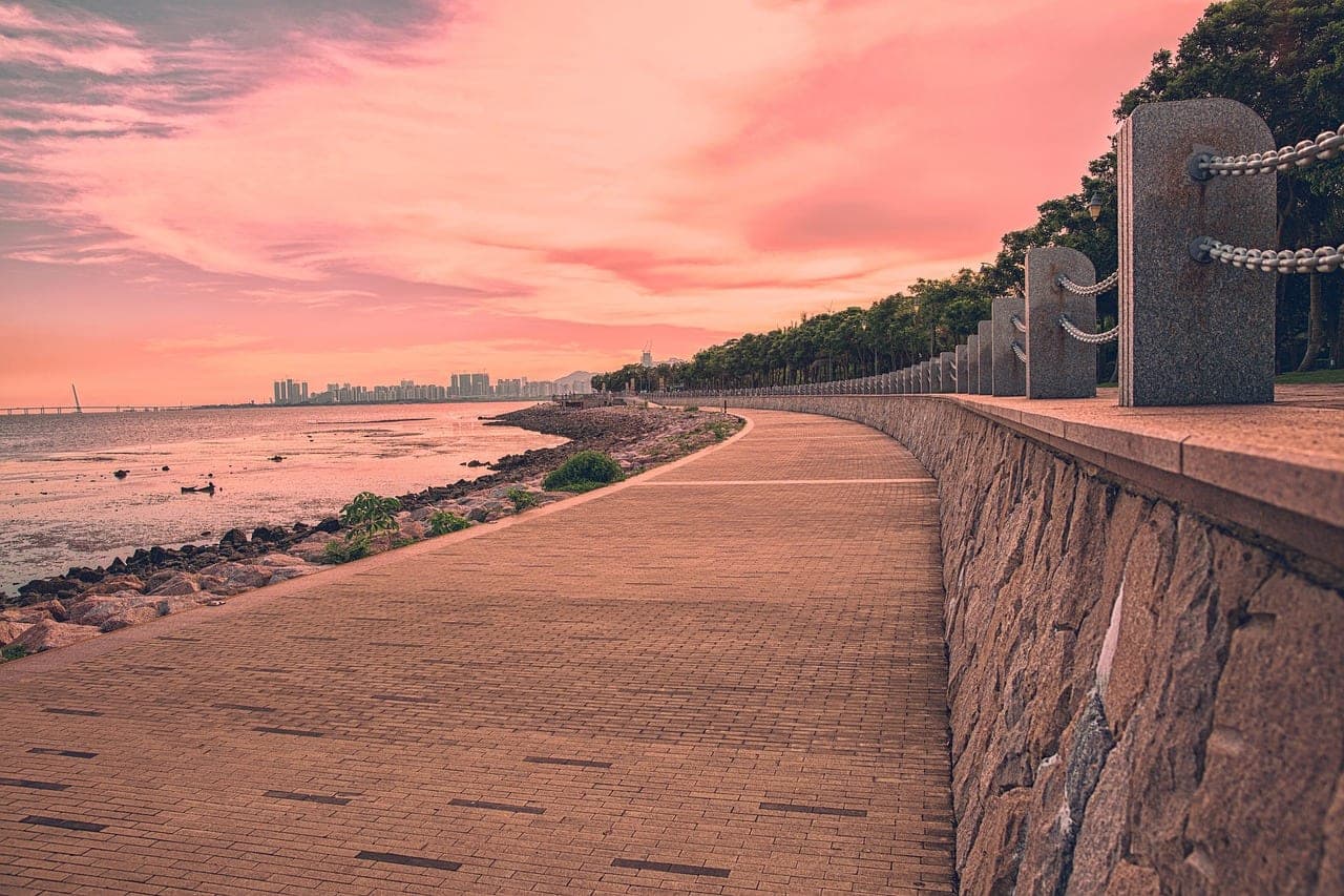 A paved seafront promenade at dusk, a line of towers in the distance.