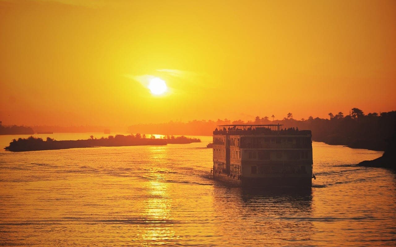 A multi-deck cruise boat moving up the river at sunset.