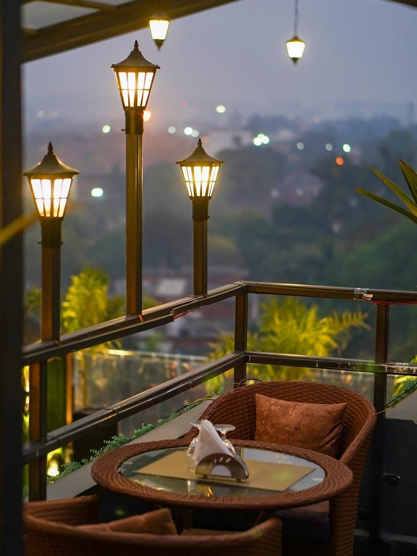 A rattan table and armchairs on a rooftop terrace, lanterns lit at dusk.