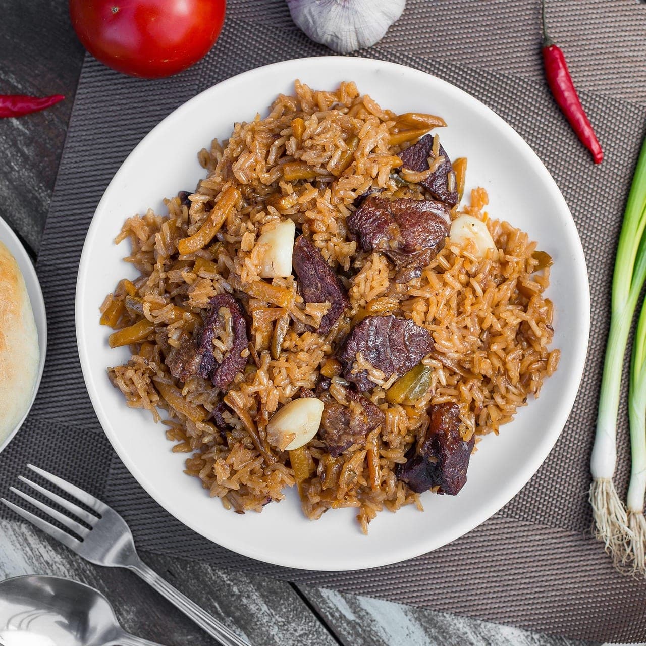 A plate of golden rice with pieces of meat and cloves of garlic.