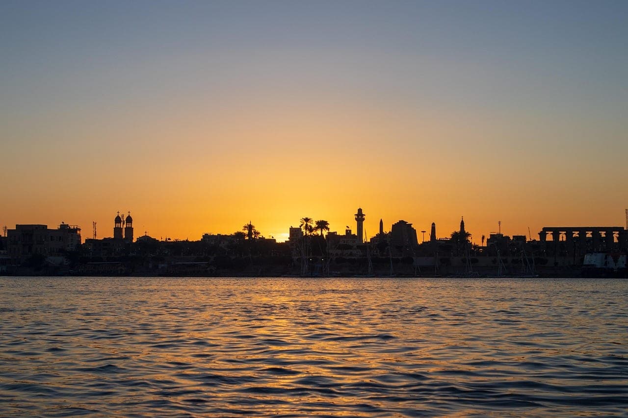 The sun sets over the Nile, the town in silhouette on the far bank.