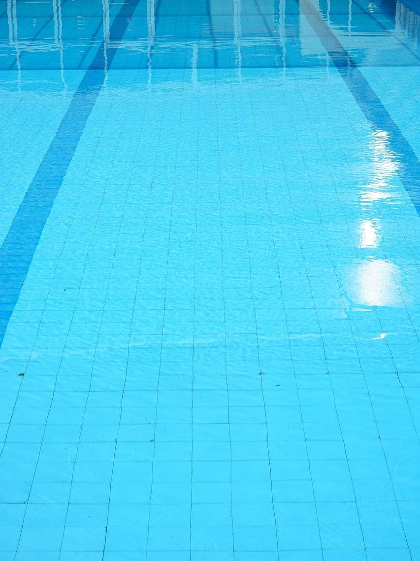 The tiled floor of a swimming pool, crossed by lane lines painted in dark blue.