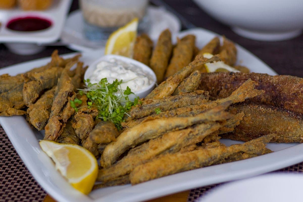 A plate of small fried fish, lemon and white sauce