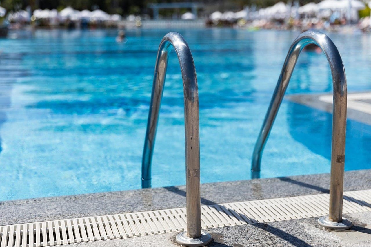 Two stainless-steel handrails at the entrance to a pool, clear water in front.