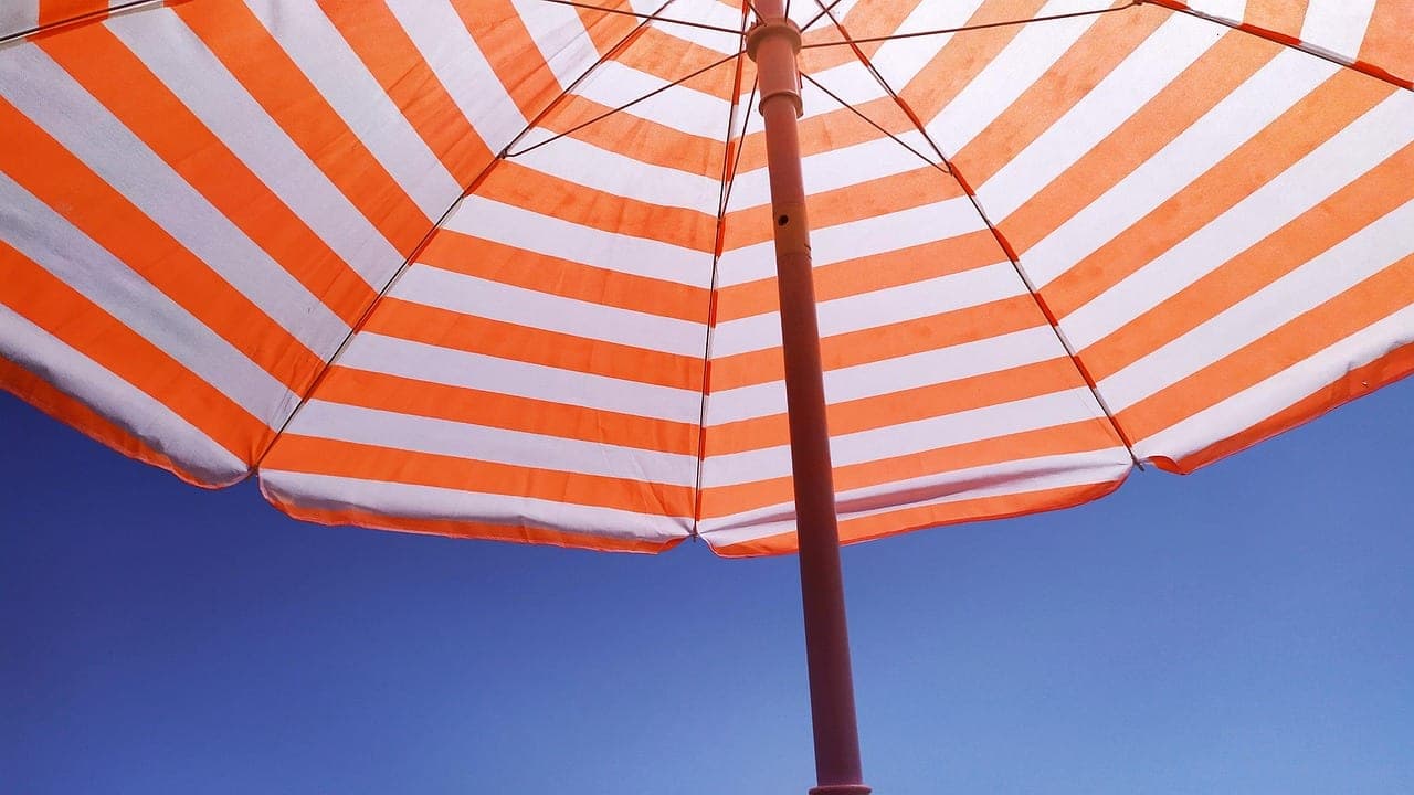 An orange-and-white striped beach parasol seen from below against a blue sky.