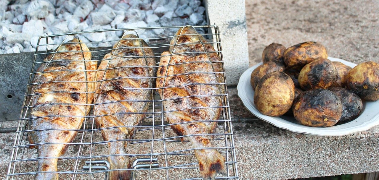 Whole fish grilled over charcoal, held in a grilling basket.