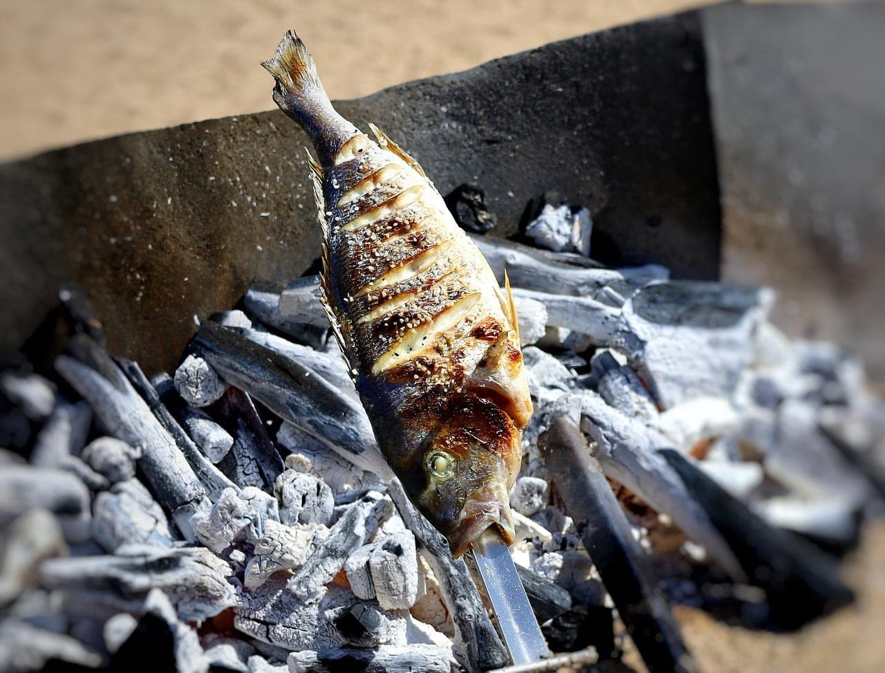A whole fish, scored and browned, resting on grey embers.