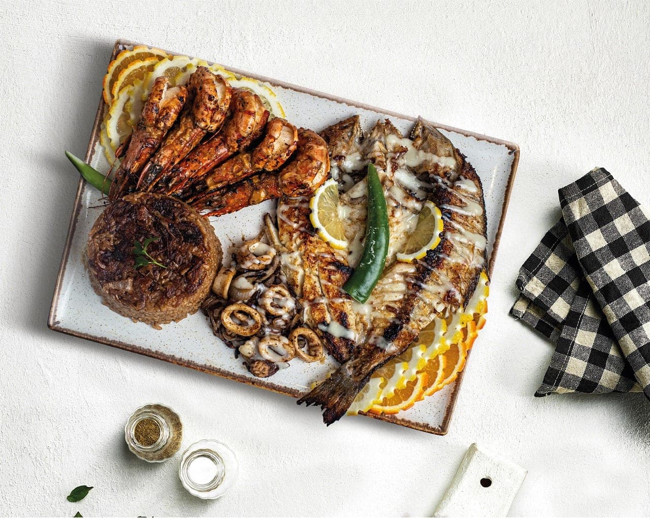 A platter of butterflied grilled fish with prawns, calamari rings, rice and lemon slices.