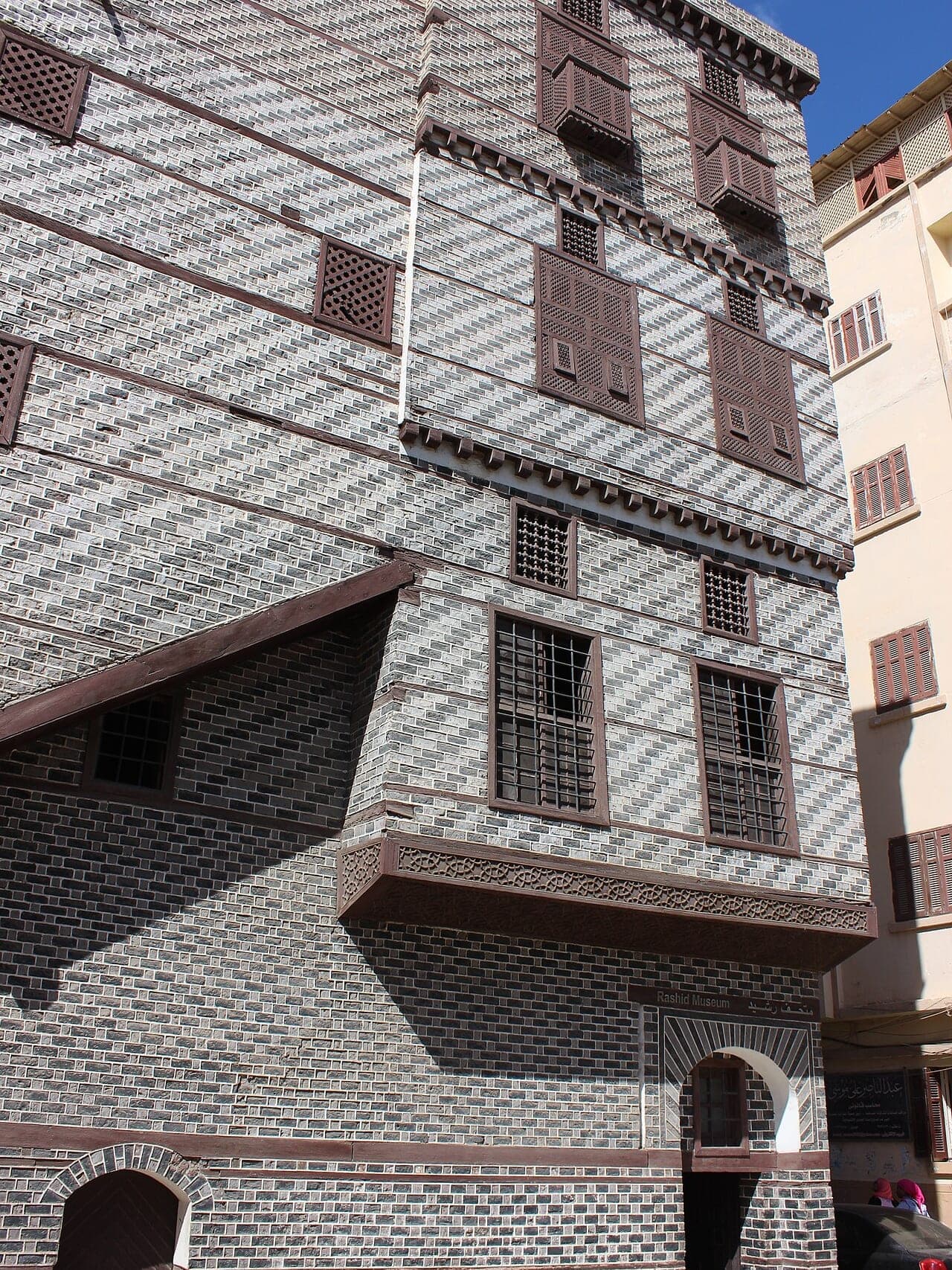 A chequerboard brick façade in black and white, pierced by wooden mashrabiya screens.