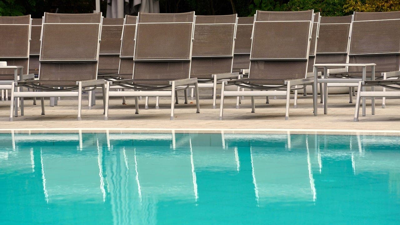 A row of empty sun loungers along a turquoise pool.