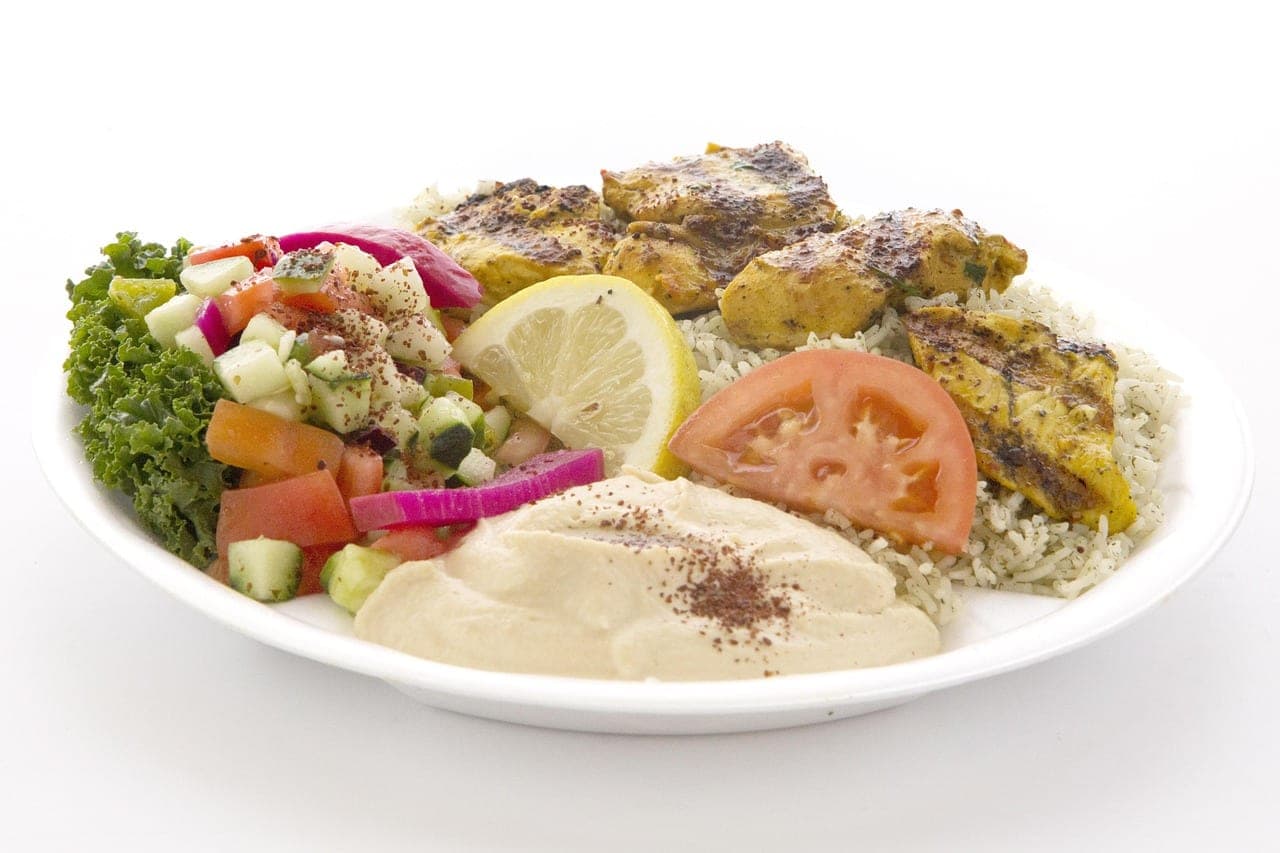 A plate of hummus dusted with sumac, grilled chicken, rice and chopped salad.