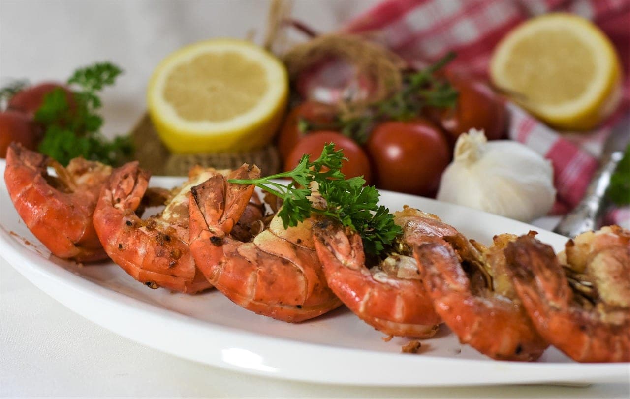 A dish of large grilled prawns with lemon, garlic and tomatoes.