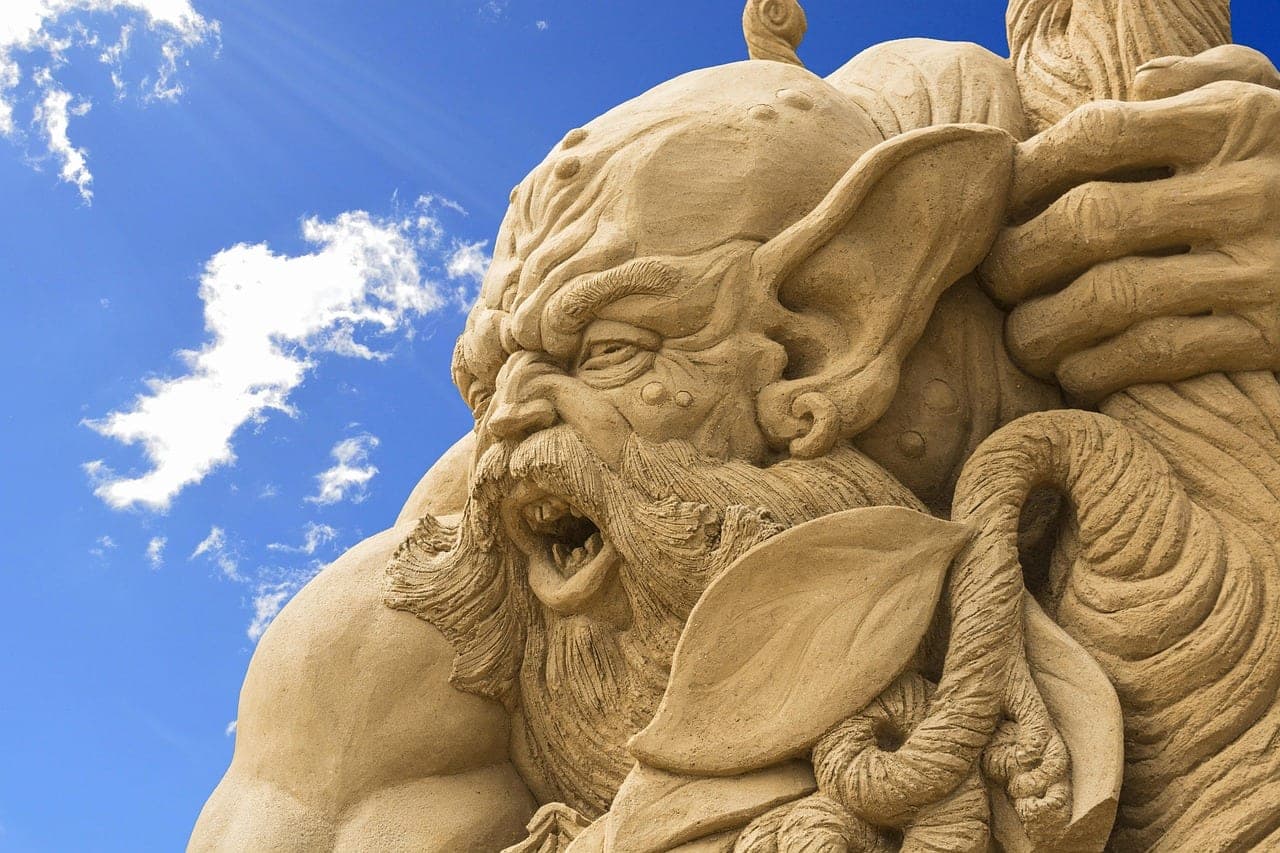 A monumental sand sculpture, a bearded face standing out against the sky.