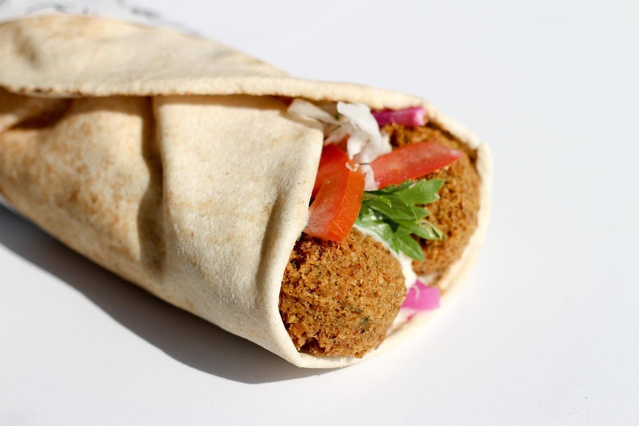 A flatbread sandwich filled with falafel balls, tomato and raw vegetables.
