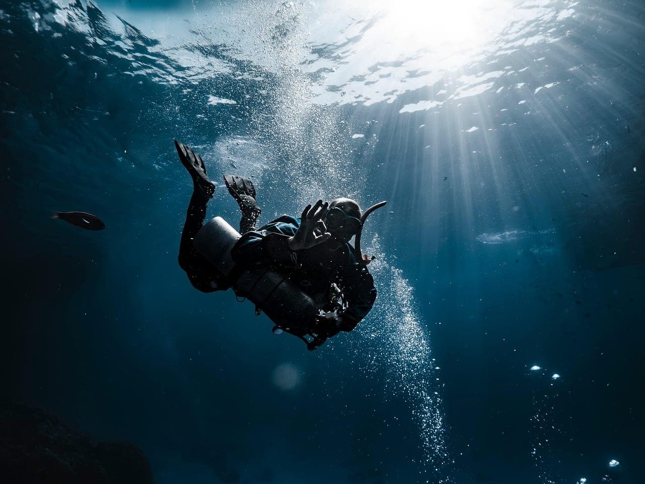 A scuba diver descends below the surface amid bubbles and shafts of sunlight.