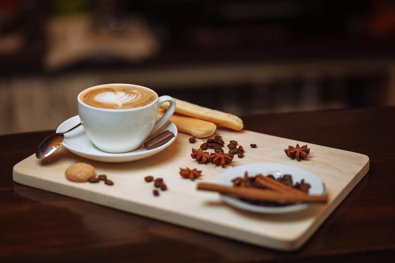 A cappuccino in a thick cup on a wooden board, with biscuits, coffee beans and cinnamon.