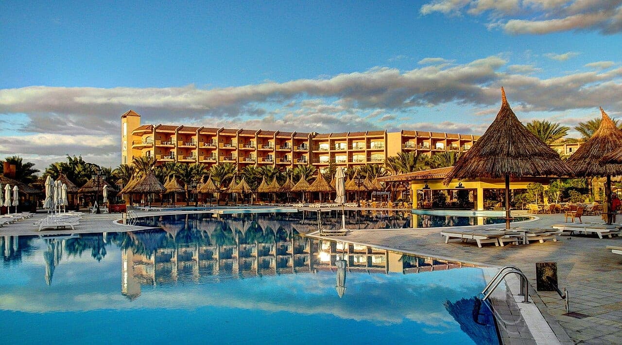 The hotel's big pool at sunset, straw parasols and ochre blocks mirrored in the water.
