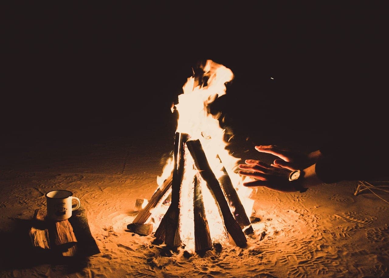A wood fire on the sand at night, hands held out to the flames.