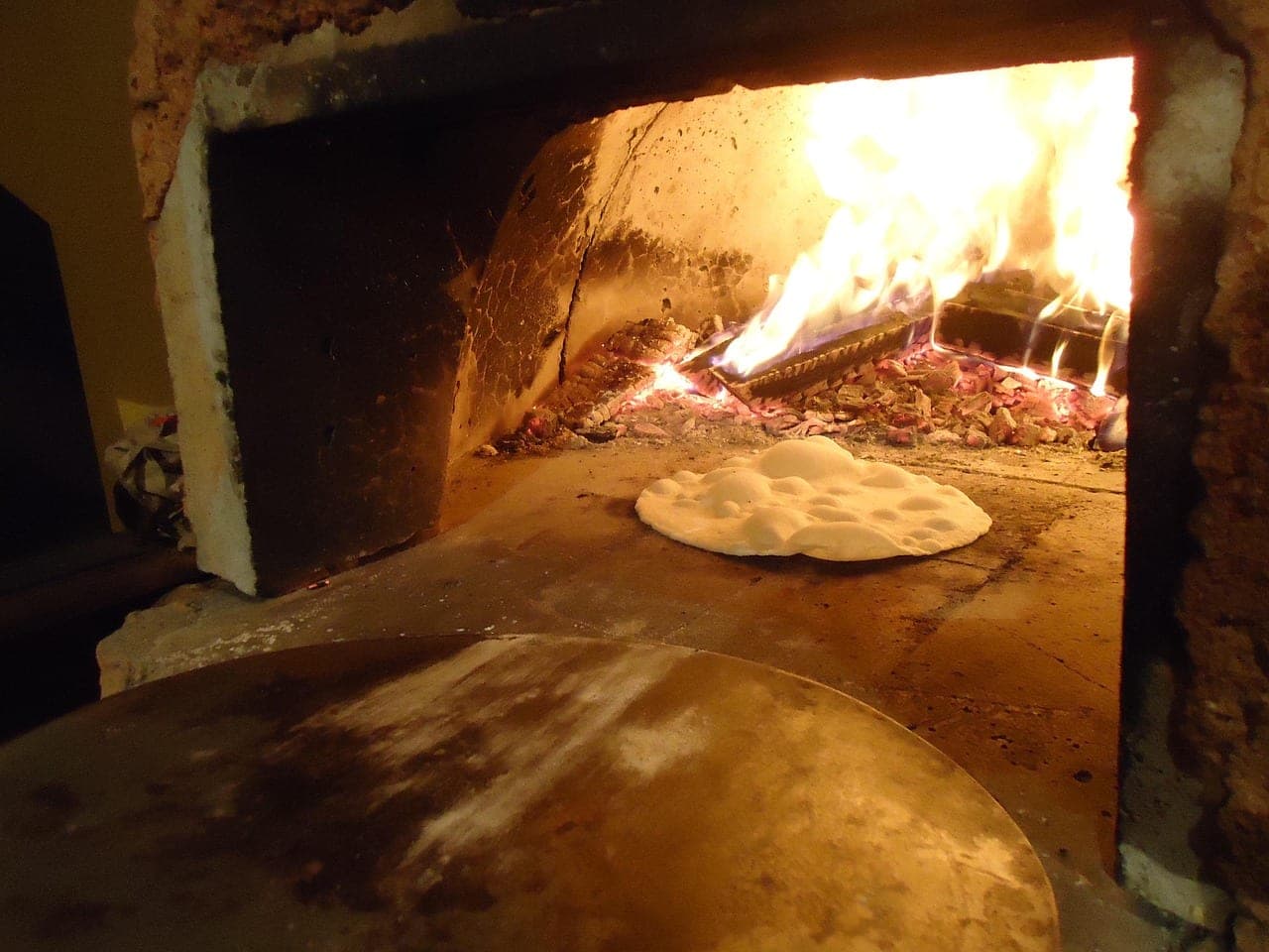 A brick oven, flames at the back and dough puffing up on the hearth.