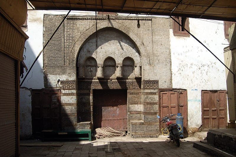 A pointed brick archway and old wooden doors in a narrow street.