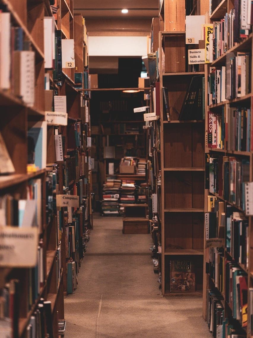 A bookshop aisle between two wooden shelves packed with books.