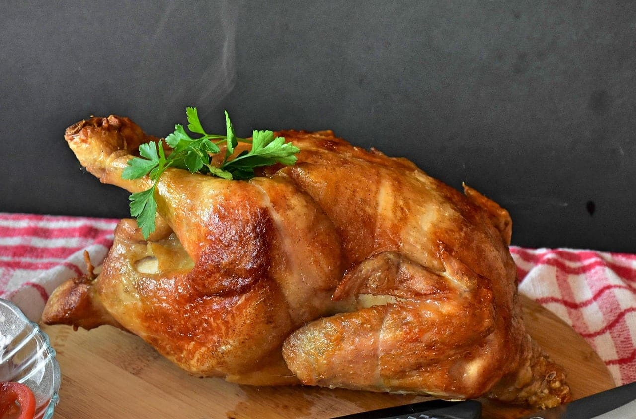 A whole roast chicken, golden and glistening, on a wooden board with a sprig of parsley.
