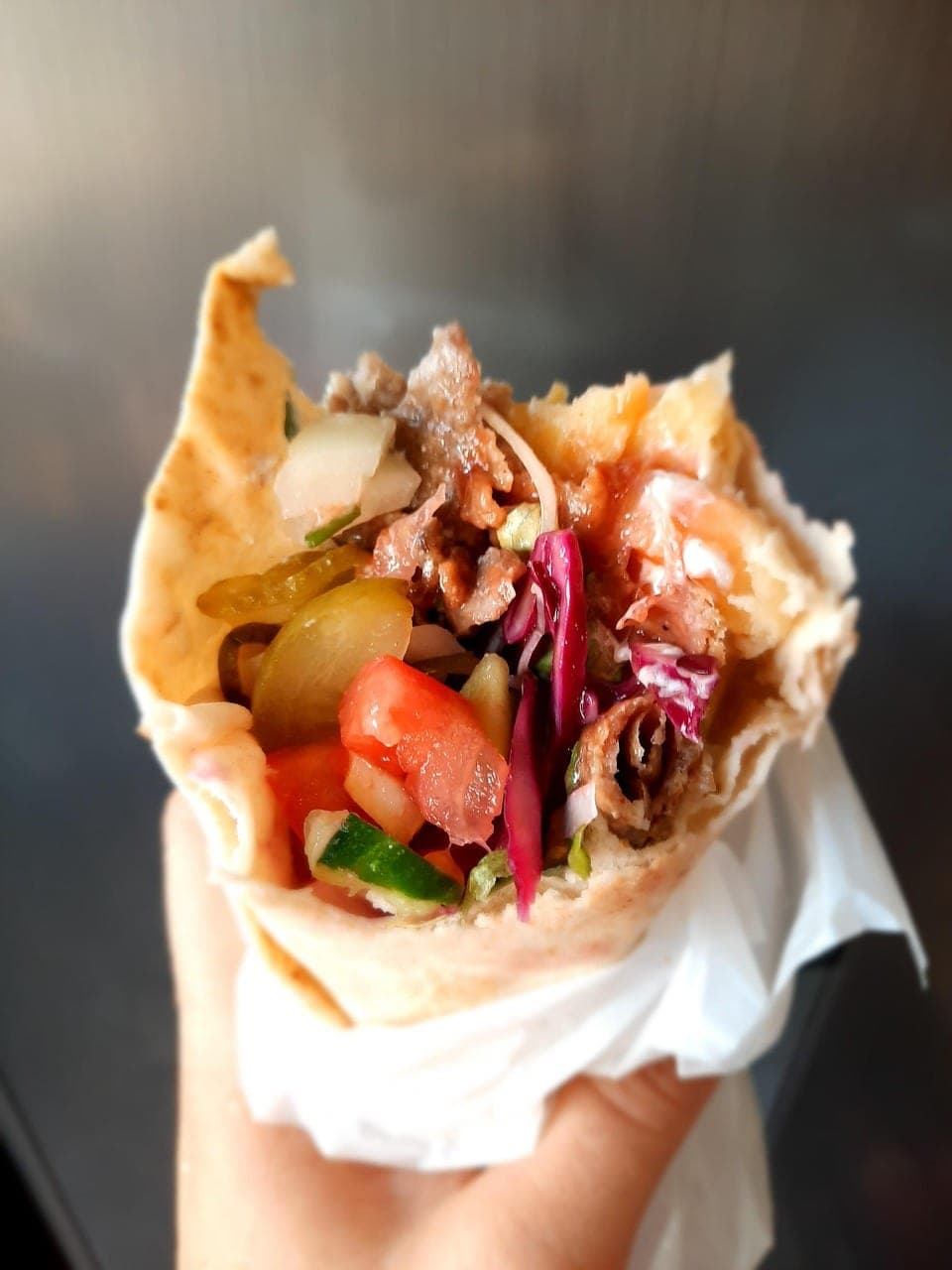A sliced-meat sandwich in flatbread, held in its paper wrapper.