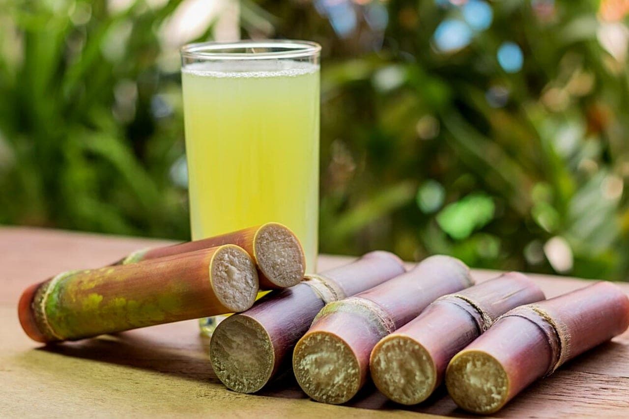 A glass of sugarcane juice in front of freshly cut lengths of cane.