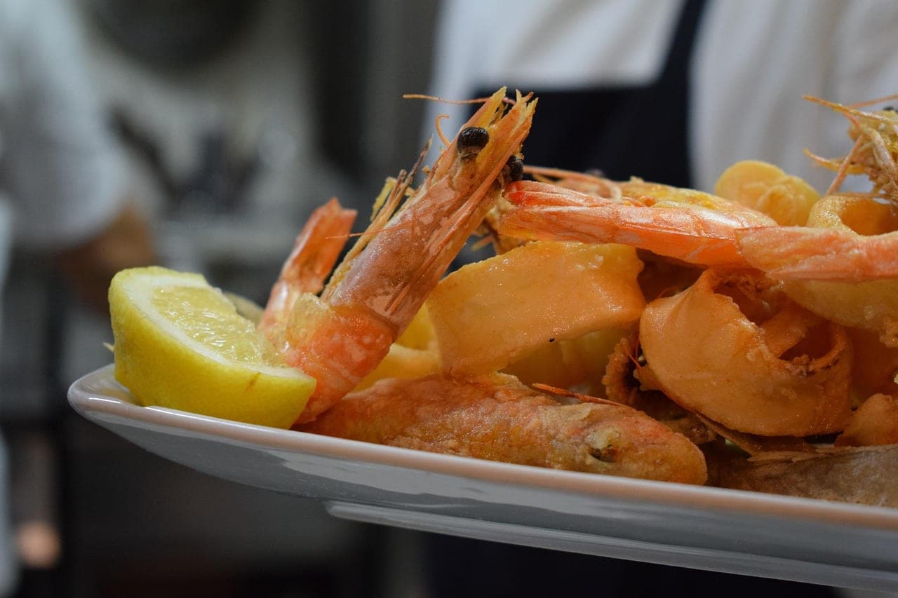 A platter of fried seafood: whole prawns, squid and a lemon wedge.
