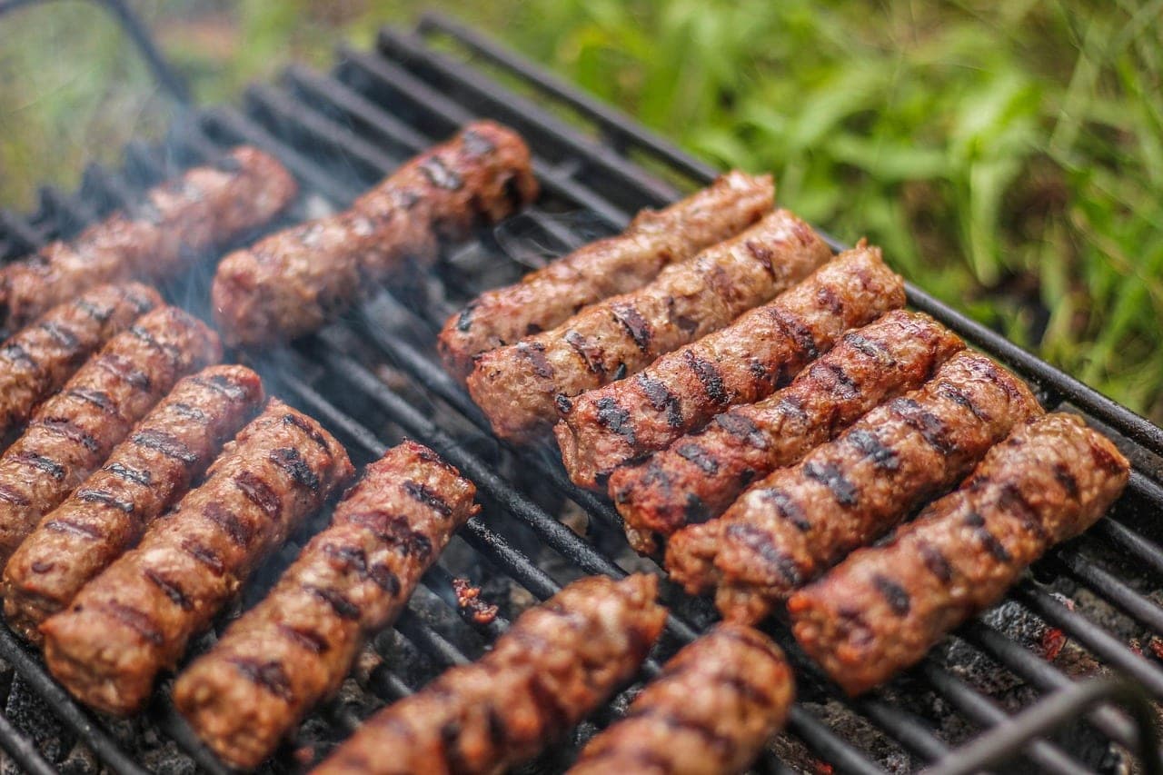 Rows of grilled minced-meat fingers on the grill, in the smoke.