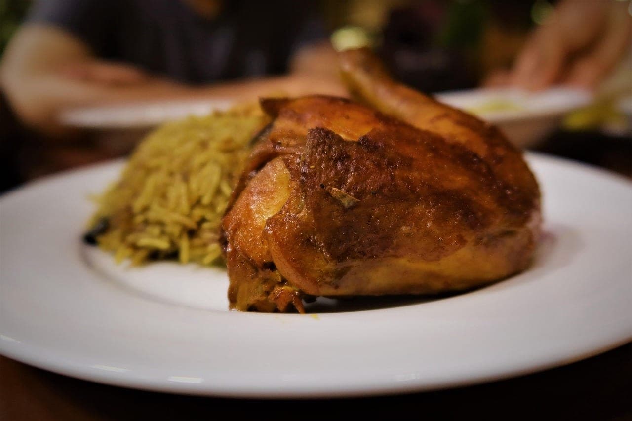 Half a roast chicken served with spiced rice on a white plate.