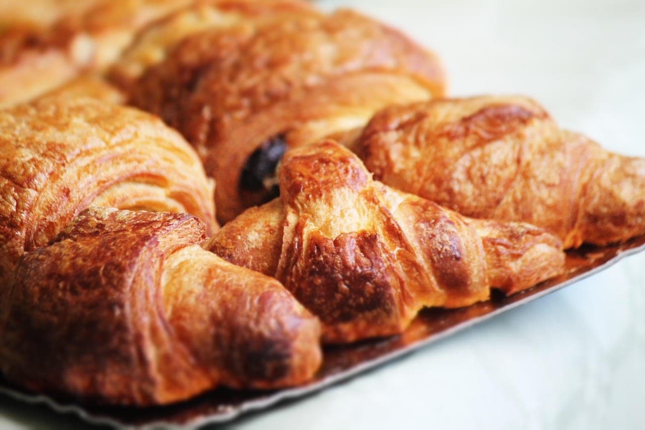 Golden croissants and a chocolate pastry crowded together on a tray.