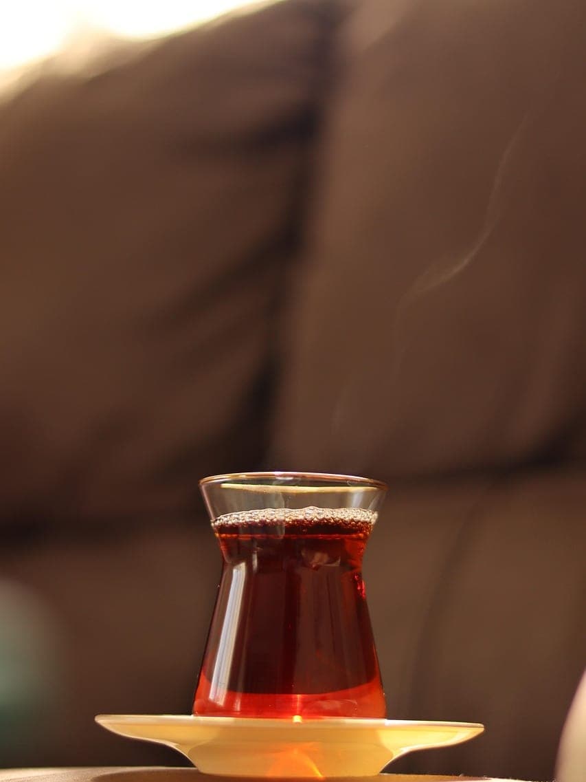 A steaming glass of black tea on its saucer, backlit.