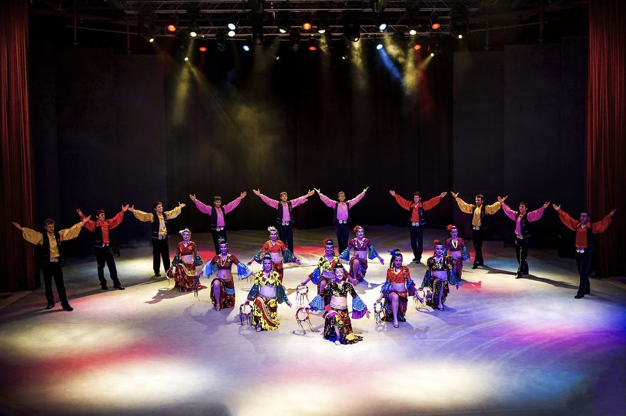 A folk dance troupe in colourful costumes on a lit stage.