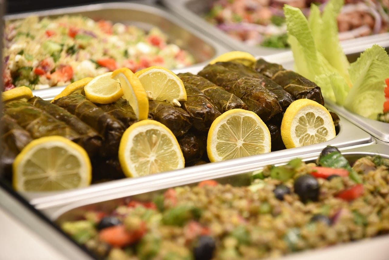 Stuffed vine leaves topped with lemon slices, between two trays of salads.